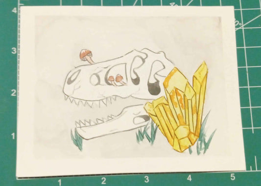 Illustration of a skull with a saw and flames on a white card, placed on a green cutting mat.