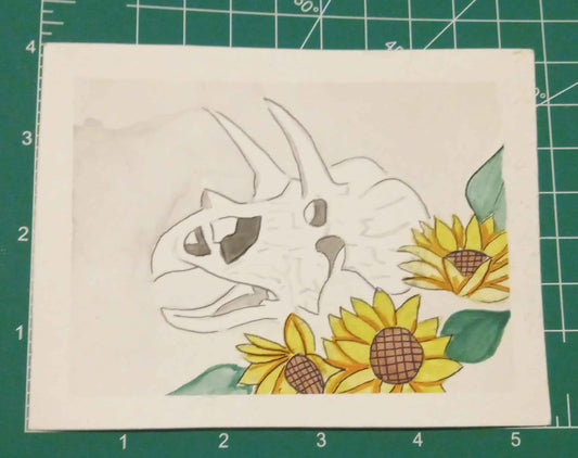 Card with a dinosaur and sunflowers design on a green cutting mat.