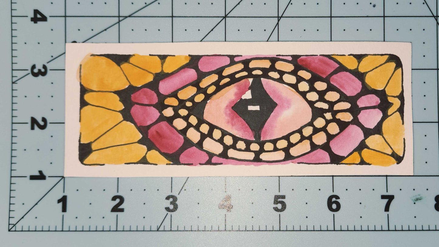 Decorative eye-shaped bookmark on a cutting mat with measurement markings