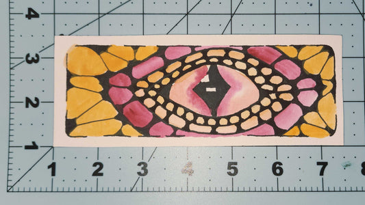 Decorative eye-shaped bookmark on a cutting mat with measurement markings