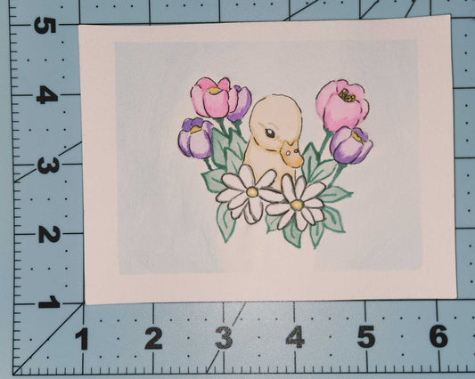 baby duck with flowers on a piece of paper, placed on a grid surface.