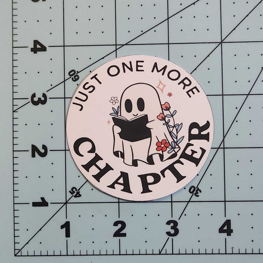 Circular sticker with text 'Just One More Chapter' on a cutting mat.