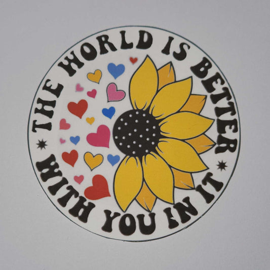 Circular design with a sunflower and hearts, featuring the text 'The world is better with you in it' on a white background.