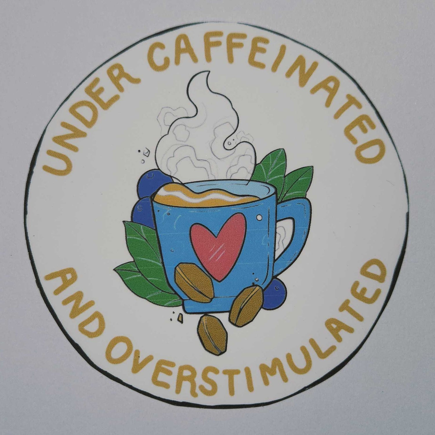 Circular logo with text 'Under Caffeinated and Overstimulated' featuring a coffee cup and heart design on a white background.
